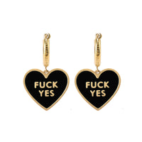 A pair of black heart-shaped earrings with the phrase 'FUCK YES' written in white letters, attached to gold-colored hoop earrings.