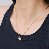 Gold necklace with a heart-shaped pendant worn by a person in a dark blue top.