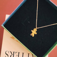 Gold gingerbread man necklace in a jewelry box on a red surface