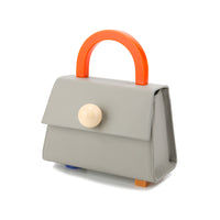 A gray satchel bag with an orange handle and a silver resin stud detail, featuring a detachable shoulder strap and a small embossed logo at the bottom.