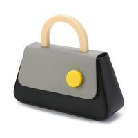 A black flap bag with a resin stud handle and a beige removable leather shoulder strap, featuring a front flap with a yellow circular logo.