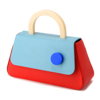 A red and blue flap bag with a strap, featuring a resin stud handle and a detachable leather shoulder strap. It has a cotton-twill interior and brushed gold hardware.