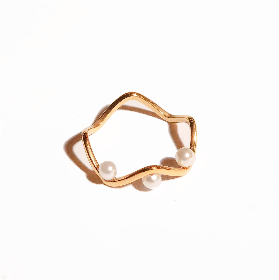 A gold-colored stainless steel ring with a smooth, curved design featuring three small pearls, intended for daily wear and resistant to tarnish.