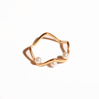 A gold-colored stainless steel ring with a smooth, curved design featuring three small pearls, intended for daily wear and resistant to tarnish.