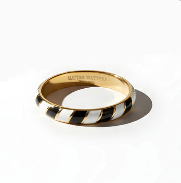 Gold enamel ring with black and white striped Memphis design on a white background