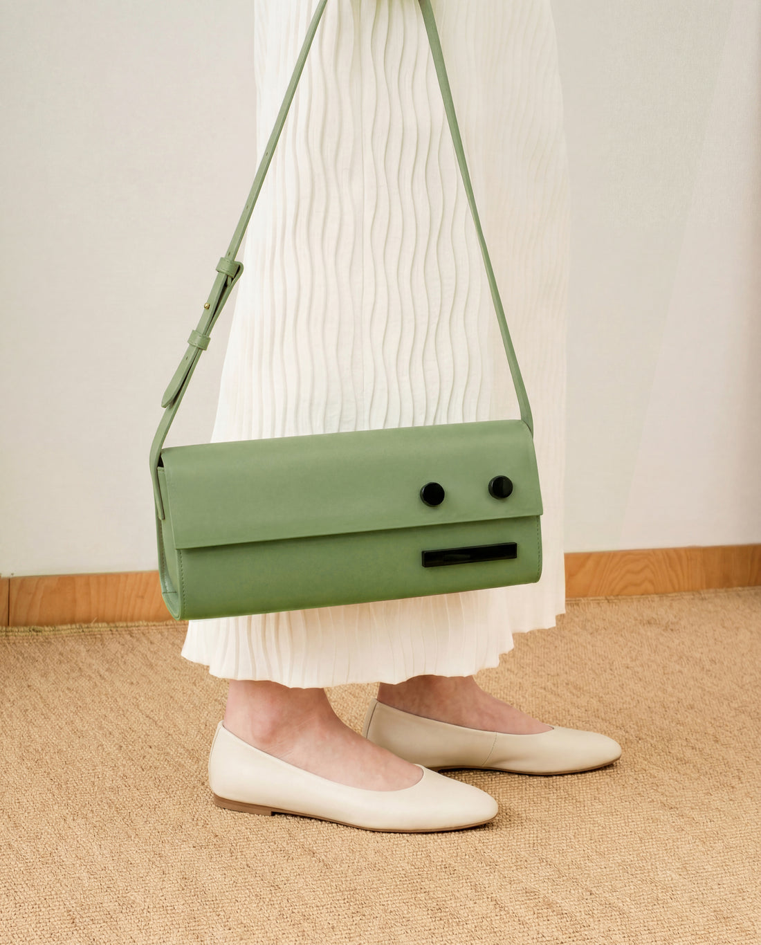 Green handbag worn over one shoulder on a person standing on a woven floor.