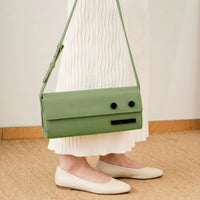 Green handbag worn over one shoulder on a person standing on a woven floor.