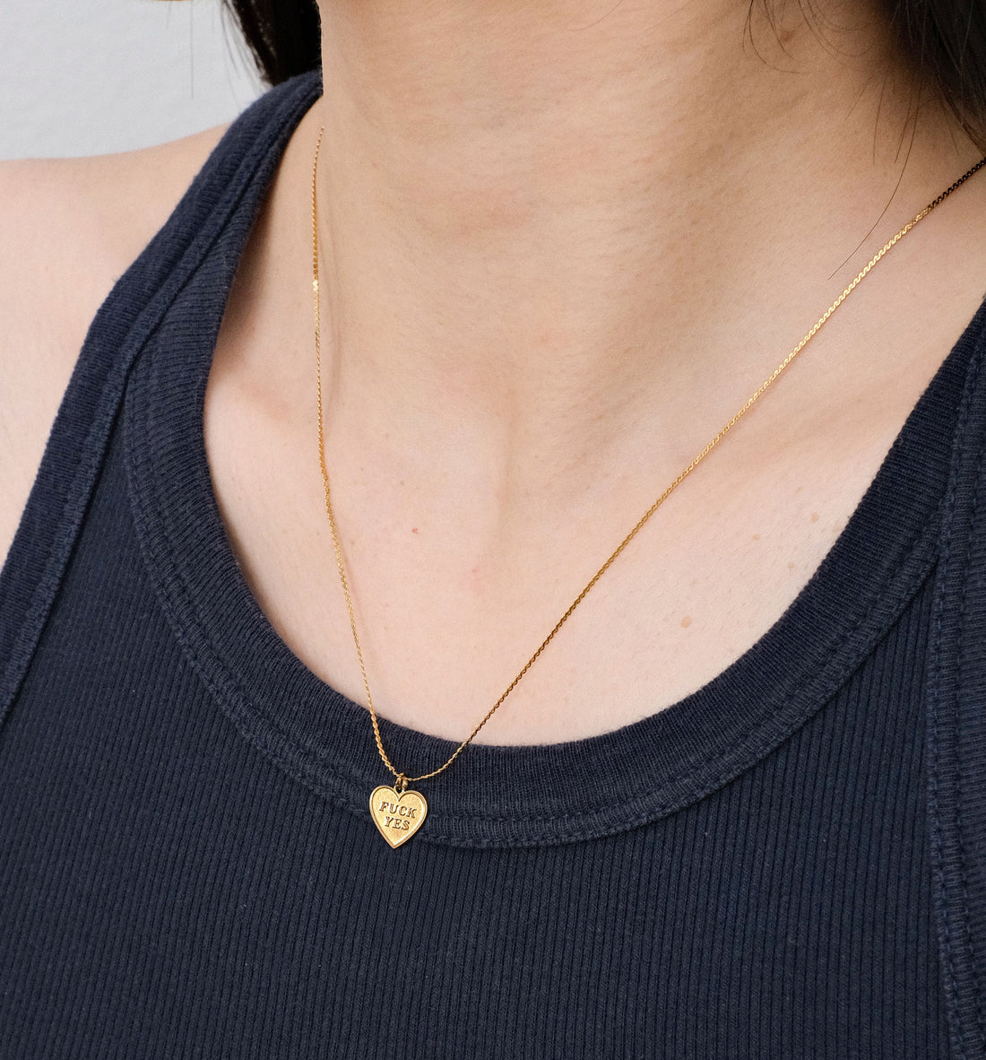 Gold necklace with a heart-shaped pendant worn by a person in a dark blue top.