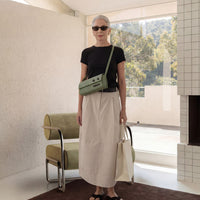 Woman standing in a modern room with a green bag and sunglasses