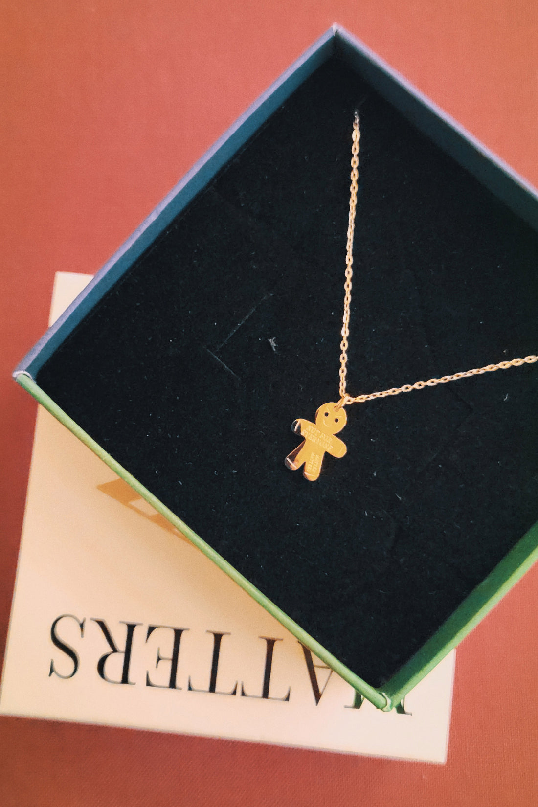 Gold gingerbread man necklace in a jewelry box on a red surface
