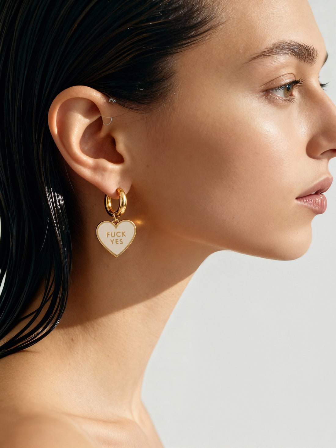 Close-up of a woman wearing a gold heart-shaped earring with text.