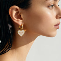 Close-up of a woman wearing a gold heart-shaped earring with text.